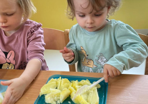 Antosia i Klaudia kroją ziemniaki za pomocą plastikowego noża.