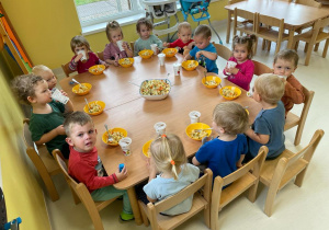 Pamiątkowe zdjęcie dzieci z grupy Żabek siedzących przy stoliku z wykonaną przez siebie sałatką warzywną.