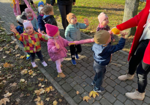 Dzieci pozujące do zdjęcia podczas jesiennej wędrówki, trzymając się spacerowej gąsienicy.