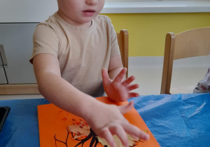 Maciej przykleja na pomarańczową kartkę liścia pomalowanego farbą.