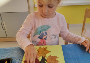 Lilianna podczas odciskania liścia pomalowanego farbą na szablonie drzewa.