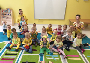 Dzieci i opiekunki ubrane na żółto pozują do zdjęcia.