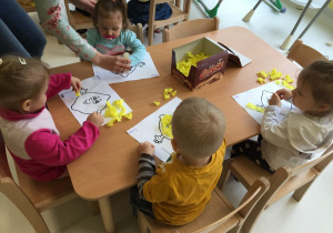 Dzieci wyklejają bibułą obrazek cytryny.