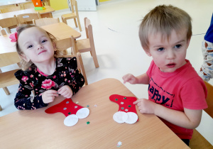 Nela i Tymon przyklejają kolorowe śnieżynki na czerwony szablon skarpety.