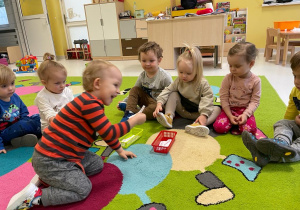 Oliwier siedzący na dywanie pośród innych dzieci losuje kartkę z wróżbą.