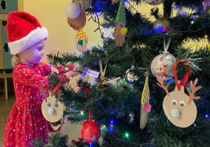 Laura w mikołajkowej czapce ozdabia świąteczne drzewko.