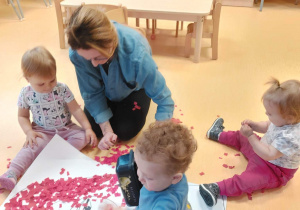 Dzieci razem z opiekunkami dekorują czerwoną bibułą wspólną pracę plastyczną - postać Czerwonego Kapturka.
