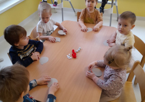 Dzieci z grupy Biedroneczki siedzące przy stole czekają na rozpoczęcie zajęć plastycznych.