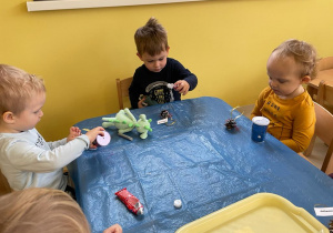 Dzieci z grupy Żabki siedzące przy stoliku tworzą swoje brokatowe ozdoby na choinkę.