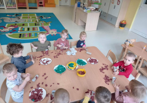 Dzieci z grupy Pszczółki siedzące przy stoliku podczas wykonywania pracy plastycznej pt. ,,Bibułowe Choineczki''.