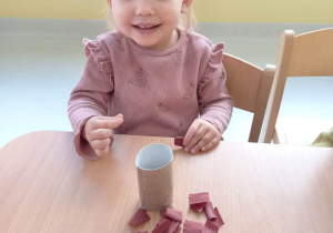 Uśmiechnięta Lilianka pozuje do zdjęcia podczas dekorowania swojej rolki papieru brązową bibułą.