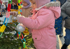 Kasia zawiesza bombkę na świąteczne drzewko.
