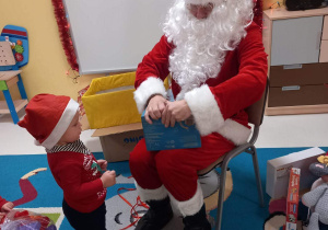 Święty Mikołaj pomaga Hubertowi rozpakować prezent.