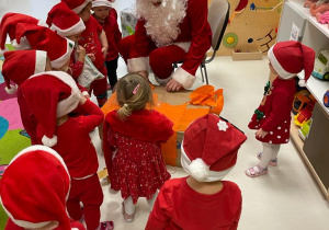 Święty Mikołaj wraz z dziećmi otwiera pudło z prezentami.