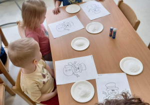 Zdjęcie dzieci z grupy Pszczółki przy stoliku przed rozpoczęciem pracy plastycznej.
