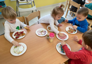 Dzieci siedzące przy stole podczas ozdabiania swoich słodkich wypieków.
