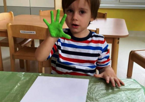 Maksymilian pozuje do zdjęcia z pomalowaną rączką na kolor zielony.