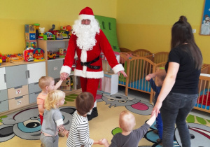 Dzieci z grupy Biedroneczki wraz z opiekunką tańczą w kole ze Świętym Mikołajem.