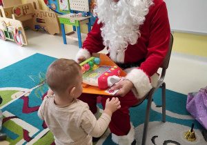 Święty Mikołaj pomaga Hubercikowi wyciągnąć nową zabawkę z opakowania.