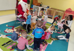 Zdjęcie Świętego Mikołaja na dywanie wręczającego dzieciom z grupy Pszczółki prezenty.