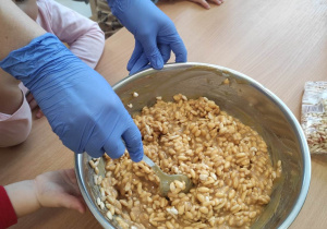 Jedna z opiekunek miesza w misce wlaną wcześniej przez dzieci masę kajmakową i ryż preparowany.