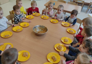 Fotografia dzieci przy stoliku z talerzykami, na których znajduje się porcja wymieszanej masy z ryżem.