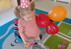Zdjęcie Zuzi trzymającej w rączkach kolorowe balony i papierową czapeczkę.