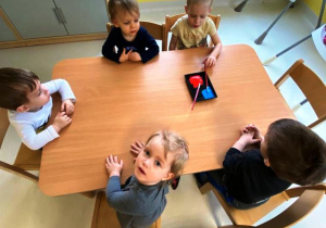 Dzieci z grupy Biedroneczki siedząc przy stoliku czekają na zajęcia plastyczne.