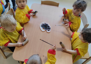 Dzieci z grupy Pszczółki siedzące przy stoliku i przygotowujące się do malowania papierowych pingwinków.