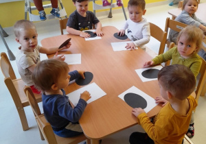 Dzieci siedzące przy stole wykonują papierowe pingwinki.
