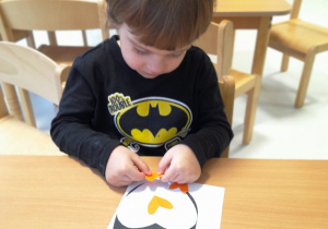 Maksymilian przykleja do swojego papierowgo zwierzątka pomarańczowy dzób i nóżki.