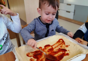 Aleksander smaruje pizzę passatą pomidorową.