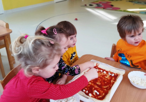 Kilkoro dzieci posypuje serem mozzarella drożdżowe ciasto.