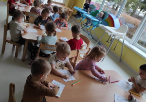 Dzieci z grupy Pszczółki siedzące przy stoliku podczas malowania kredkami torcików urodzinowych z okazji 4-tych Urodzin Żłobka.