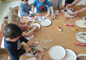 Zdjęcie dzieci podczas dekorowania swoich serduszek różnymi ziarenkami.