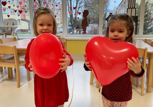 Antosia i Zuzia pozują do zdjęcia trzymając czerwone balony w kształcie serca.
