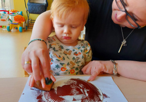 Jedna z opiekunek pomaga Wojtusiowi pomalować swojego pączka za pomocą gąbeczki.
