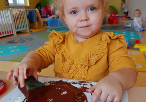 Laurka z grupy Motylki podczas malowania swojego papierowego pączka gąbeczką namoczoną w brązowej farbie.
