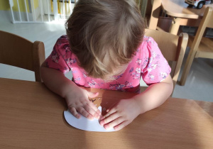 Skoncentrowana Alicja przykleja na swojego pączka, wycięty z białej kartki szablon pełniący rolę lukru.