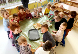 Dzieci z grupy Biedroneczki stojące wokół dużego stolika, na którym leżą produkty spożywcze.