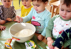 Zdjęcie dzieci przyglądających się Helence dodającej kolejny składnik do ciasta.