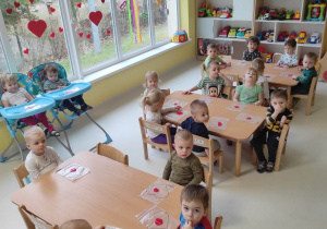 Grupowe zdjęcie dzieci siedzących przy stoliku podczas oczekiwania na rozpoczęcie zajęć plastycznych.