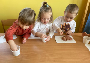 Troje maluchów przy stoliku wykonuje pączki z masy solnej.