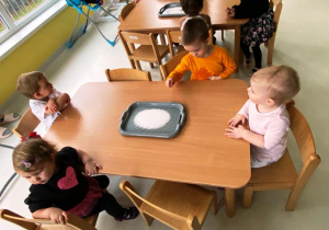 Zdjęcie dzieci siedzących w czasie zajęć przy stole, na którym leży taca z solą.