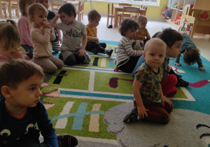 Zdjęcie dzieci siedzących na dywanie podczas oglądania bajki edukacyjnej.