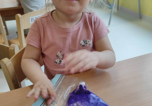 Zdjęcie uśmiechniętej Zuzanny podczas malowania fioletową farbą swojego ślimaka.