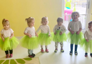 Dziewczynki z grupy Biedroneczki w zielonych spódniczkach stojące w półkolu tuż przed występem tanecznym dla chłopców z grupy.