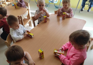 Zdjęcie dzieci siedzących przy stoliku, podczas otwierania otrzymanych od Oliwiera soczków w kartonikach.