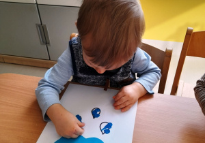 Fabianek wykleja niebieską plasteliną kropelki deszczu narysowane na kartce.