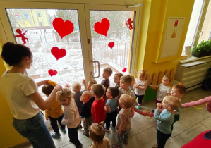 Zdjęcie dzieci obserwujących warunki pogodowe przez oszklone drzwi.